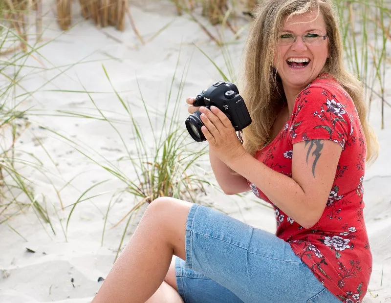 Astrid Flohr sitzt lachend mit Kamera im Dünensand