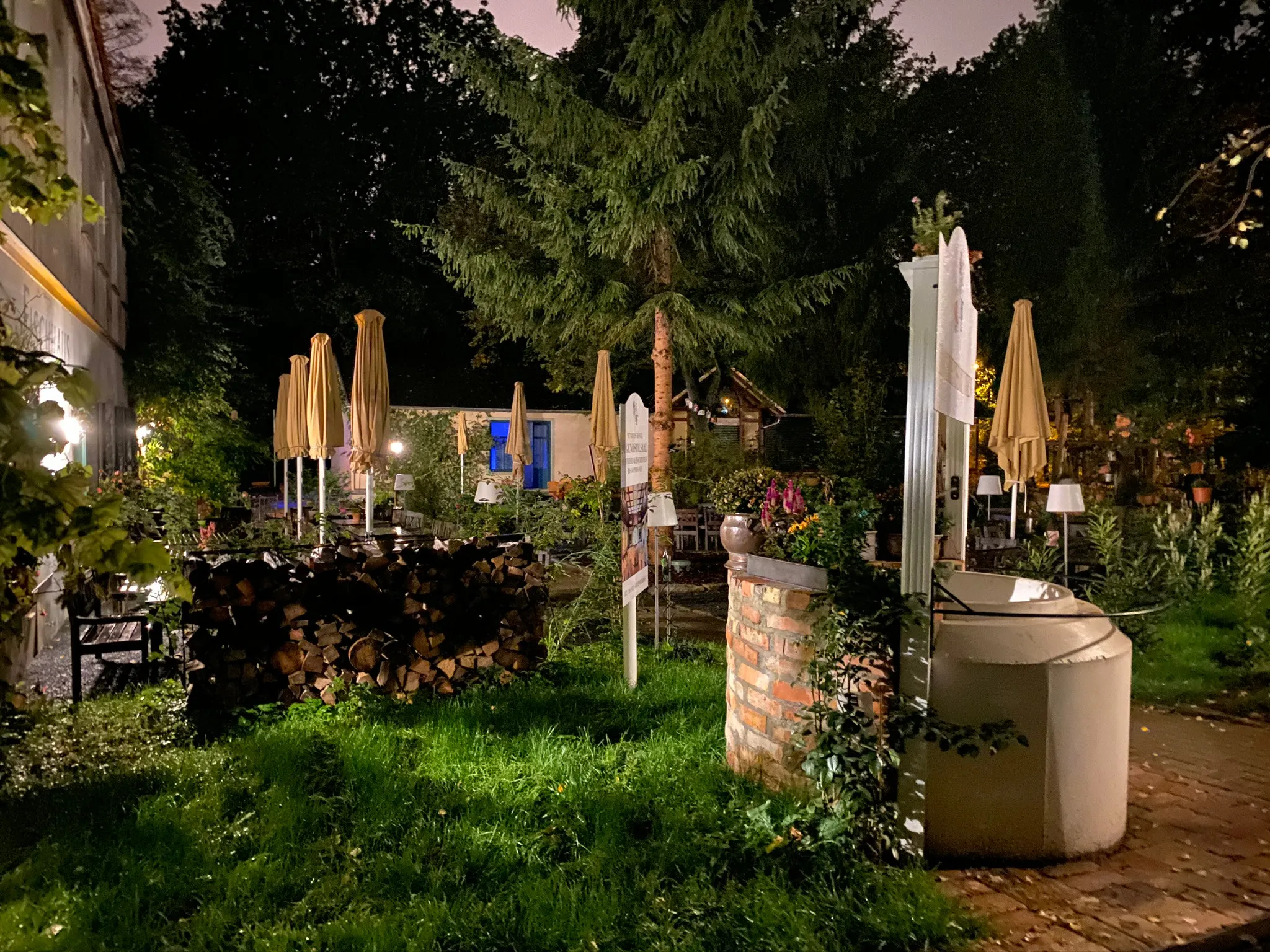 Beleuchteter Gartenbereich mit geschlossenen Sonnenschirmen am Abend