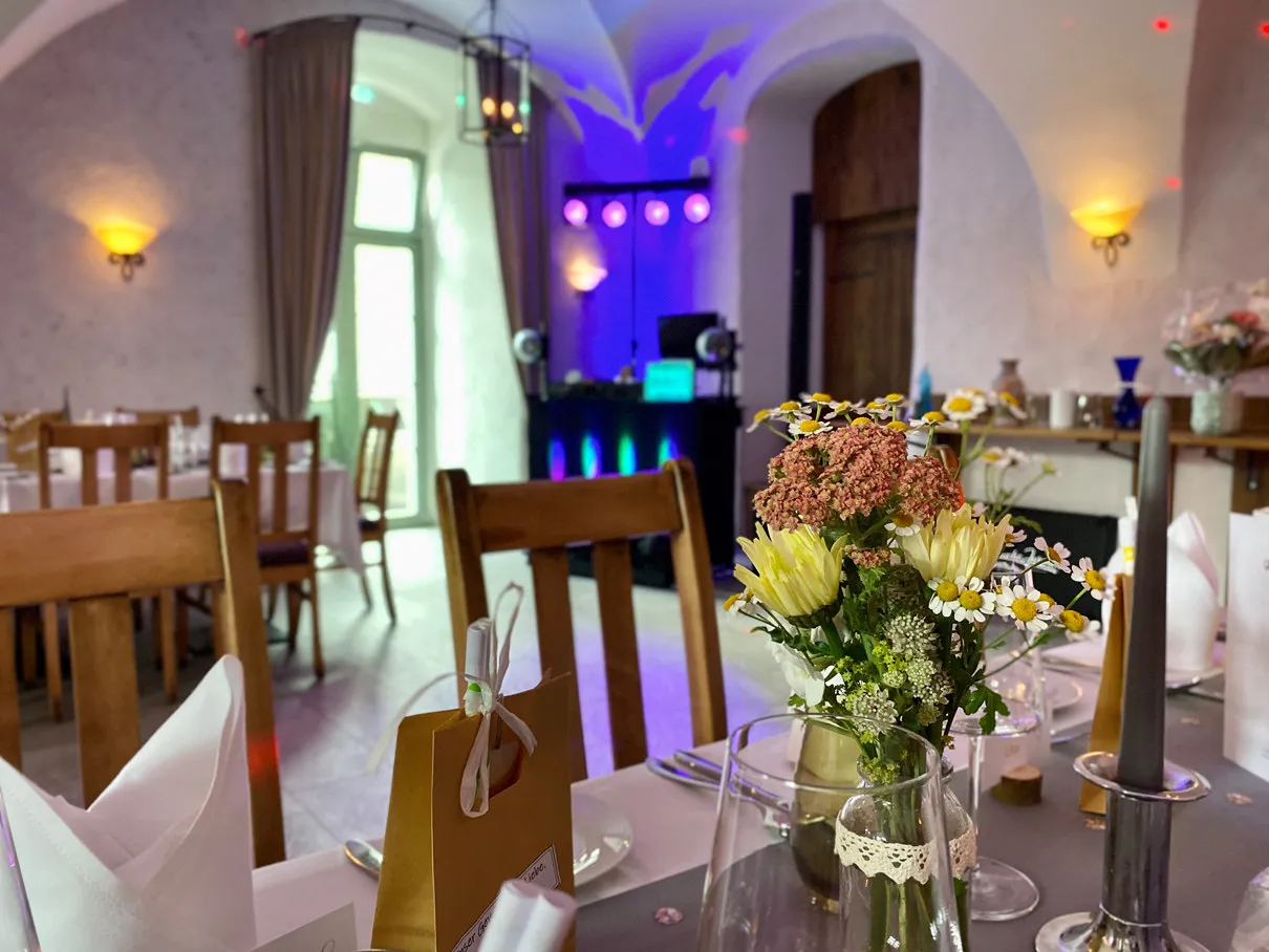 Blumenschmuck und Menükarte auf gedeckter Tafel vor DJ-Pult