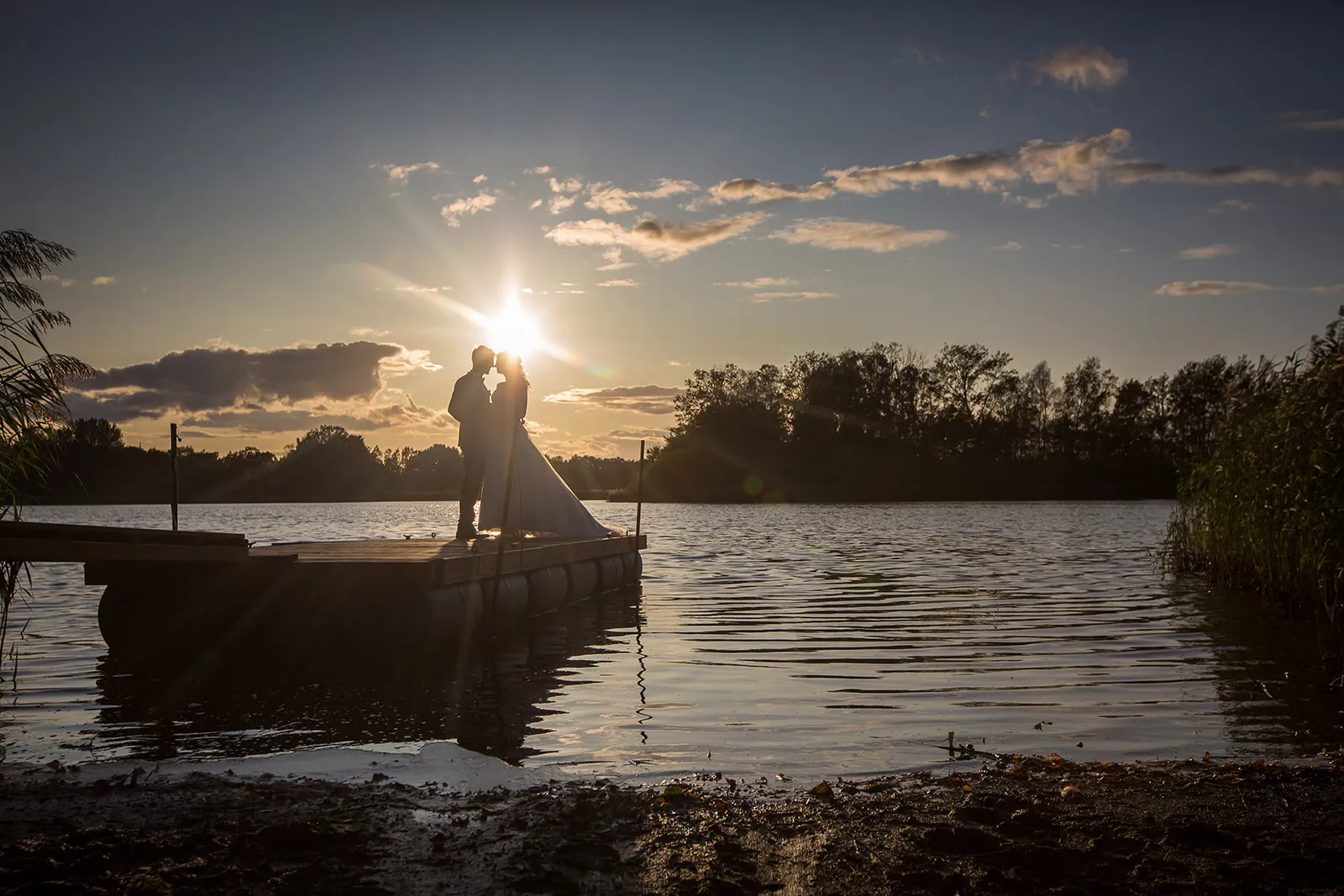 Brautpaar als Silhouette auf einem Steg im Sonnenuntergang