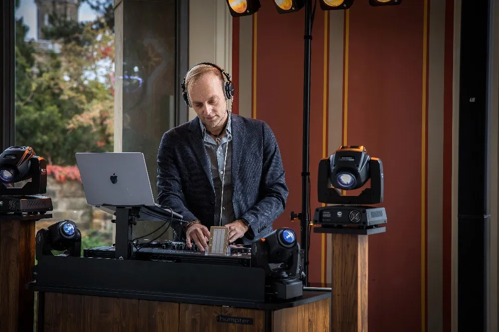 DJ Sascha Juranek beim auflegen hinter dem DJ Pult mit kopfhörern auf dem Kopf