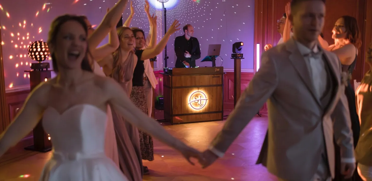 Brautpaar und Gäste tanzen vor dem DJ-Pult im Festsaal