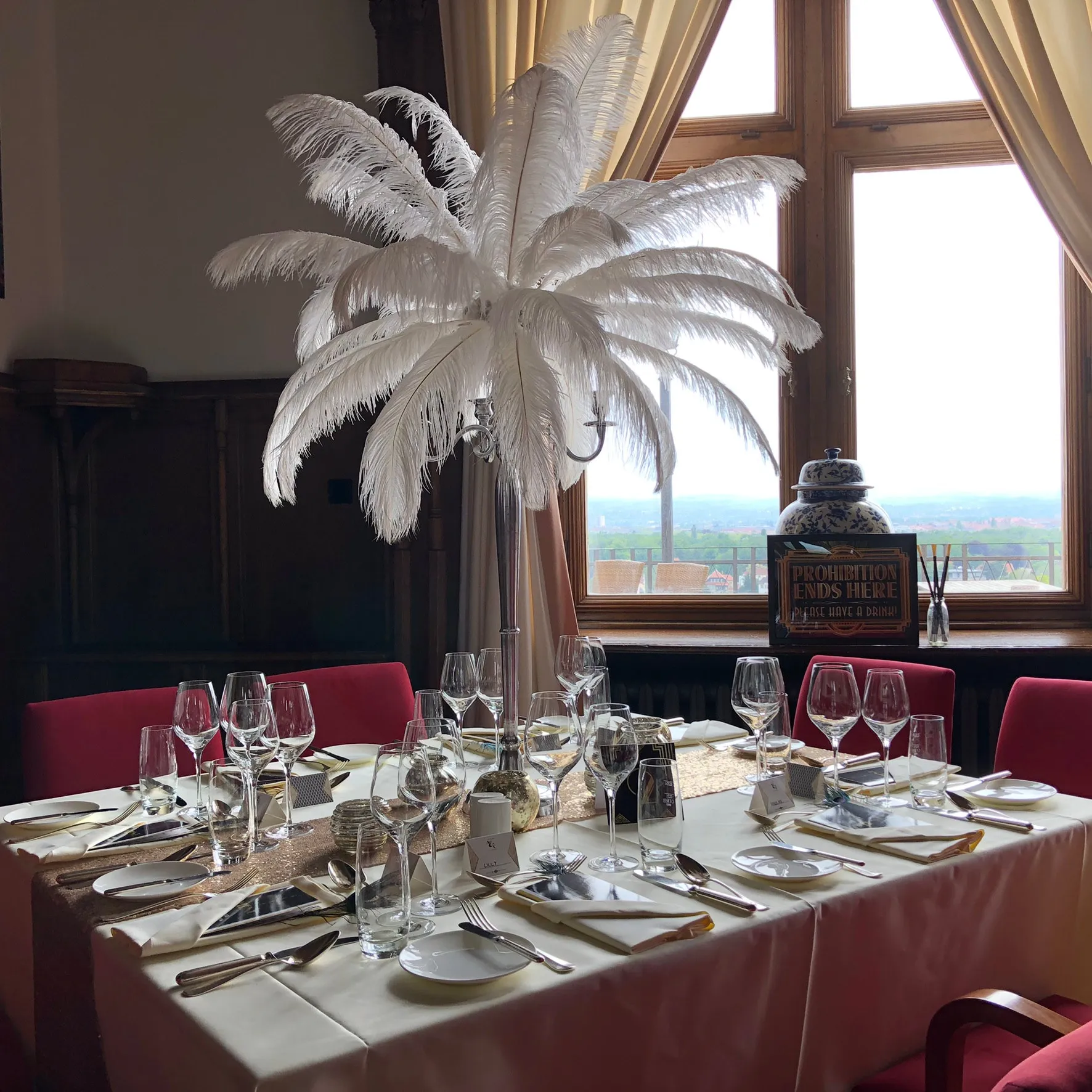 Festlich eingedeckte Tafel mit hoher Federdekoration am Fenster