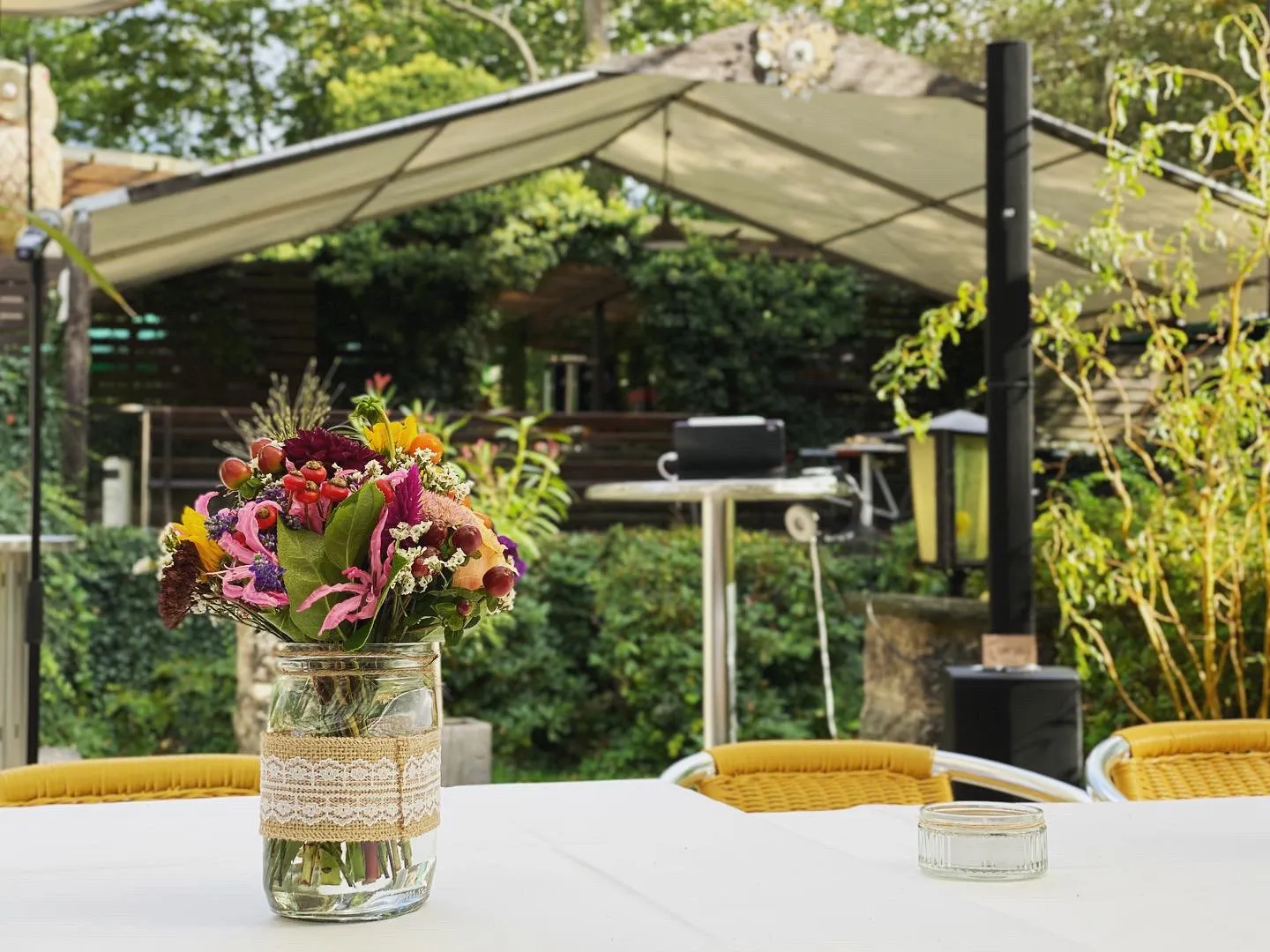 Gedeckter Gartentisch mit gelben Korbstühlen vor dem Sonnensegel