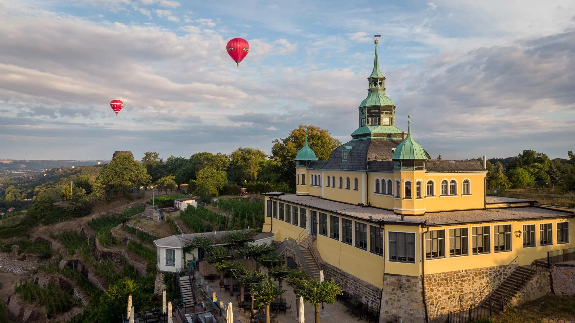 Gelbes Gebäude mit grünen Turmhauben über den Weinbergterrassen