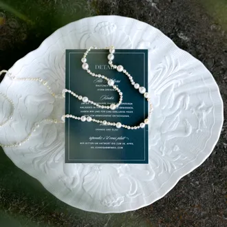 Hochzeitspapeterie mit Einladungskarte und Perlenkette auf hellem Untergrund