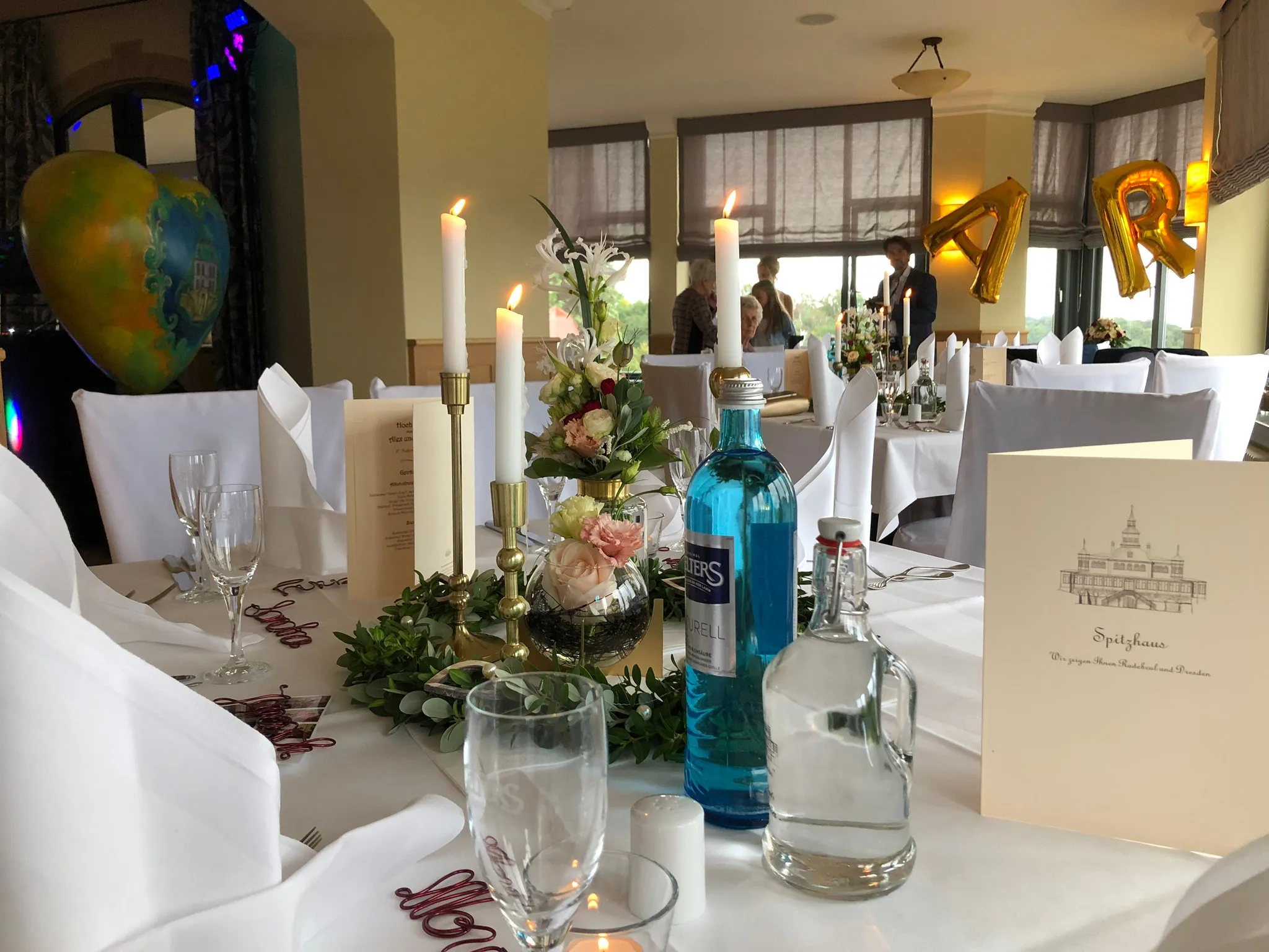 Hochzeitstafel mit brennenden Kerzen, Blumen und Ballonbuchstaben