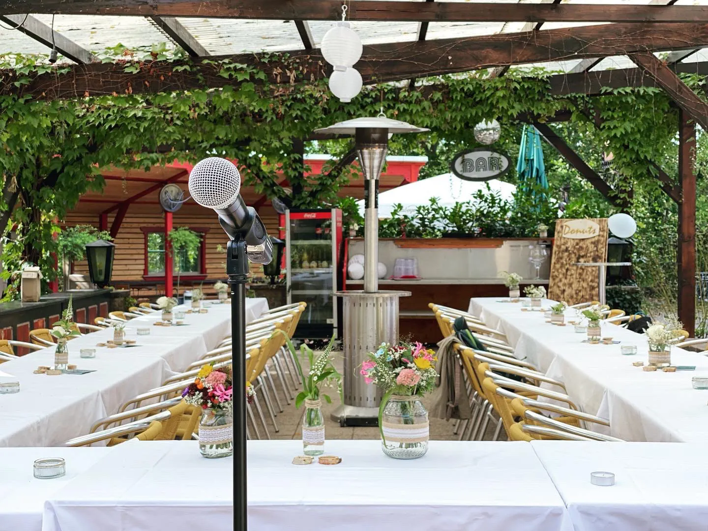 Mikrofon vor langen Tafeln unter der Pergola der Saloppe