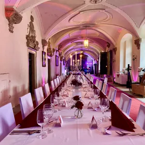 Schlossgang mit Gewölbedecke, festlich gedeckter Tafel und Ambientelicht in Rosa